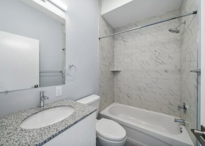Tiled bathroom with white cabinets, full-sized mirror with overhead lighting, and tub with shower
